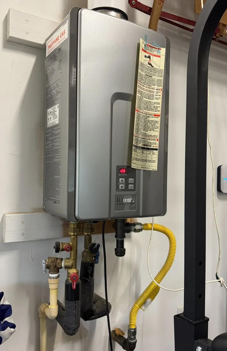 A propane tankless water heater on a garage wall, with its display on the front and the gas connection and water lines underneath